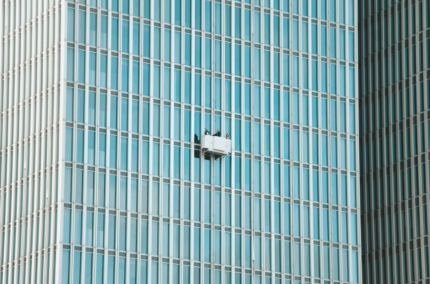 Des ouvriers sur une plateforme nettoient les fenêtres d'un immeuble de bureaux moderne.