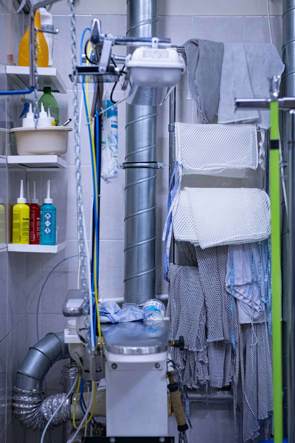 Zone de blanchisserie industrielle avec tuyaux de ventilation et produits de nettoyage.