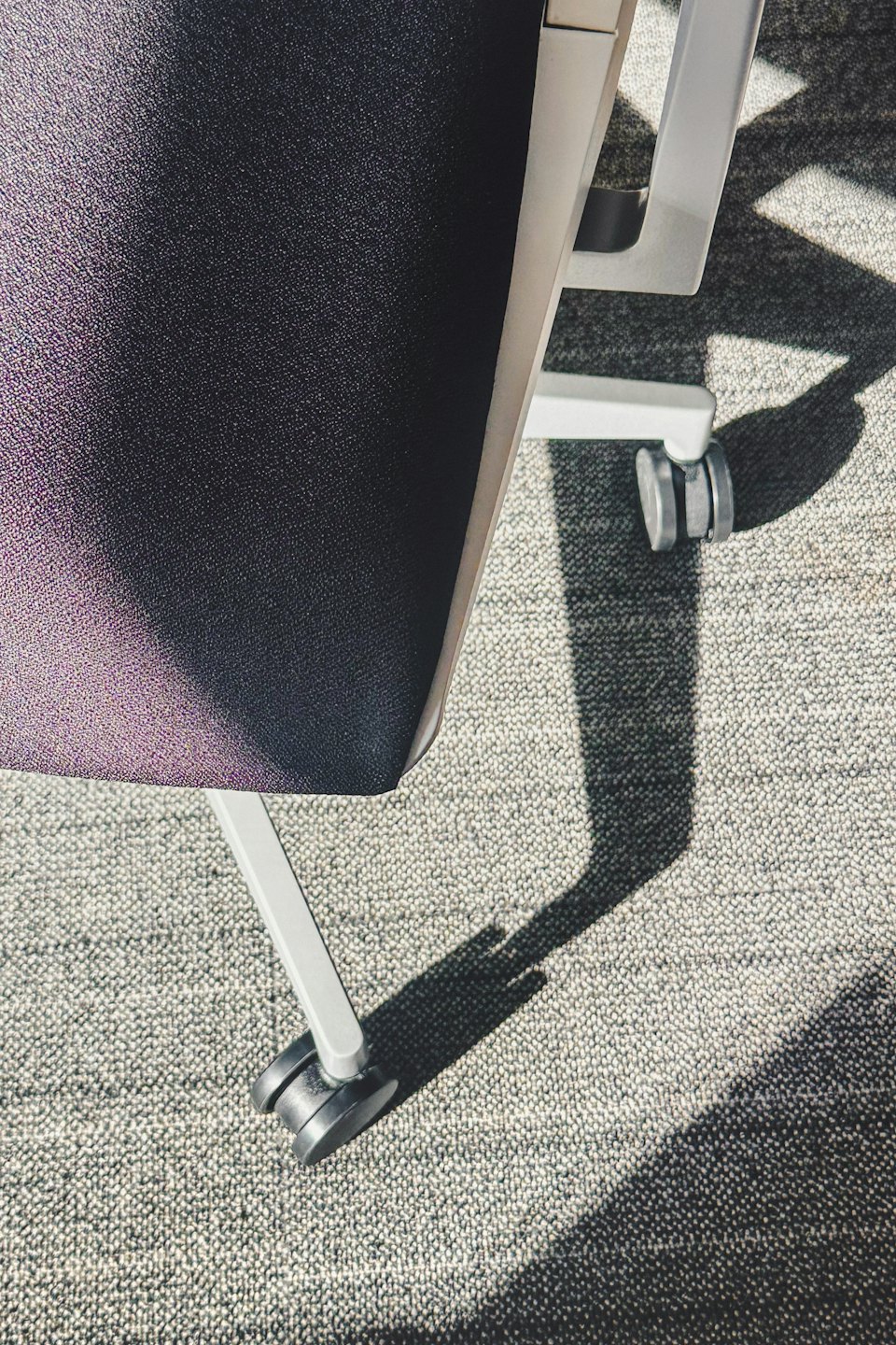 Pieds de chaise de bureau modernes avec roulettes noires sur tapis gris.
